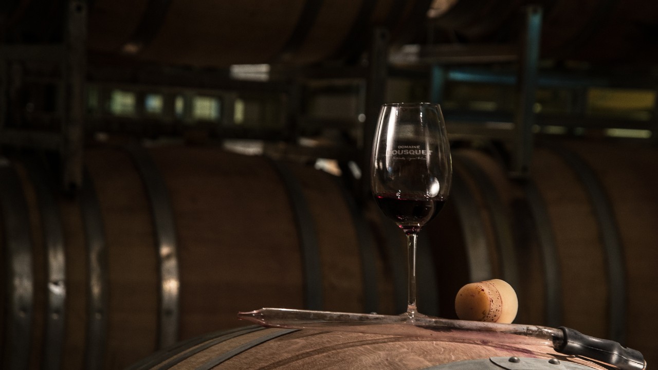 A glass of Domaine Bousquet organic wine that contains minimal sulfites perched atop a barrel.